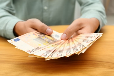 Man with Euro banknotes at table, closeup