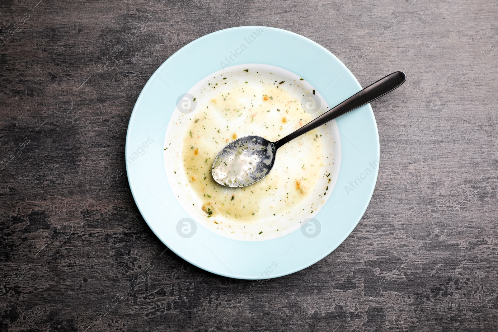 Photo of Dirty plate with food leftovers and spoon on grey background, top view