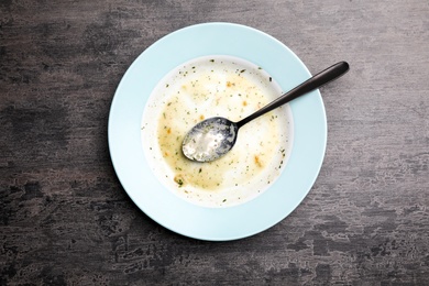 Photo of Dirty plate with food leftovers and spoon on grey background, top view