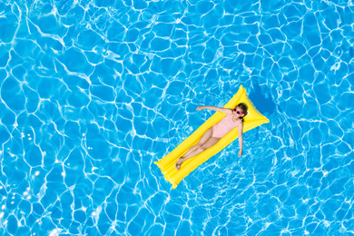 Image of Cute little girl with inflatable mattress in swimming pool, top view. Space for text 