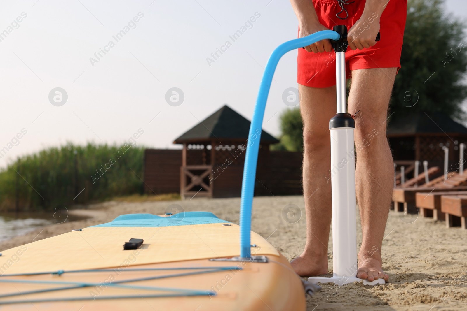 Photo of Man pumping up SUP board on river shore, closeup