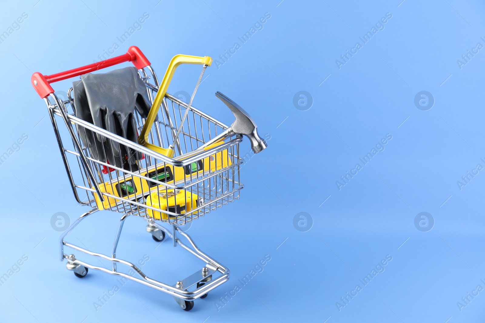 Photo of Small shopping cart with set of construction tools and gloves on light blue background. Space for text