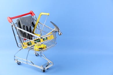 Photo of Small shopping cart with set of construction tools and gloves on light blue background. Space for text