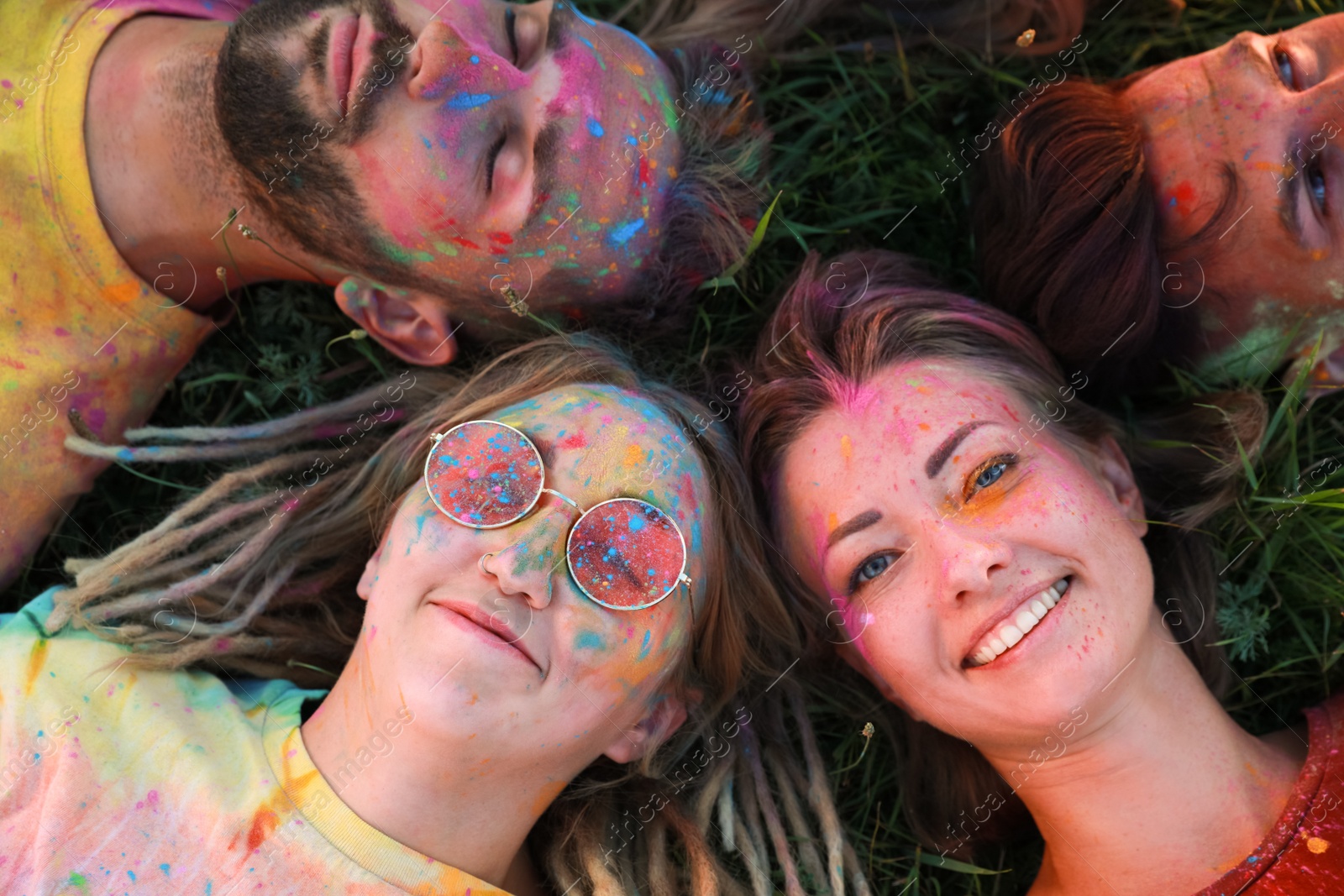 Photo of Happy friends covered with colorful powder dyes on green grass outdoors, above view. Holi festival celebration