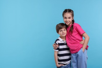 Happy brother and sister hugging on light blue background, space for text