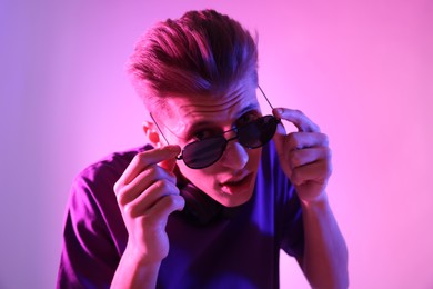 Photo of Young man with sunglasses on pink background in neon lights