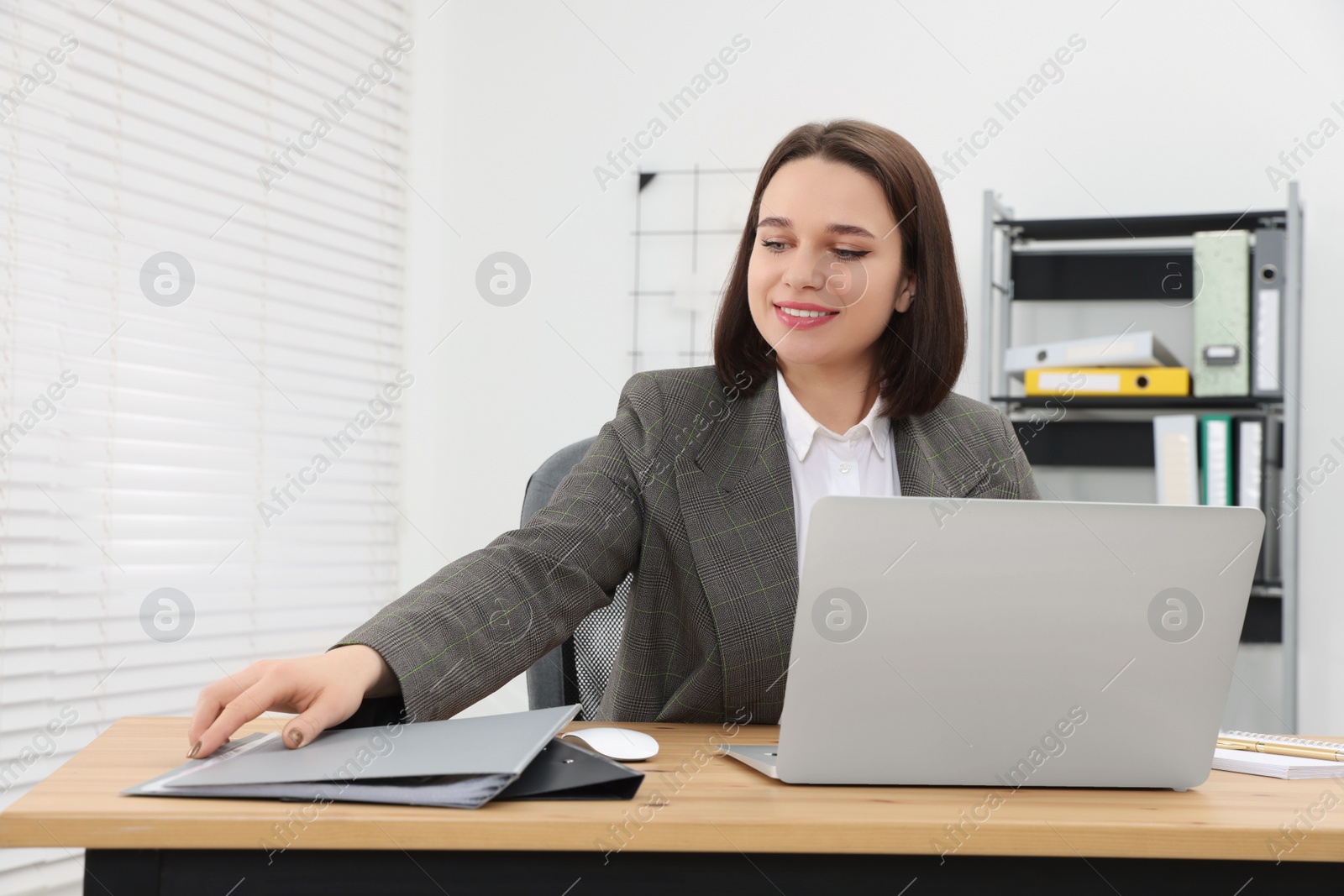 Photo of Happy young intern working with laptop at table in modern office