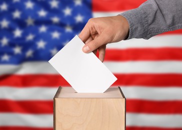 Election in USA. Man putting his vote into ballot box against national flag of United States, closeup