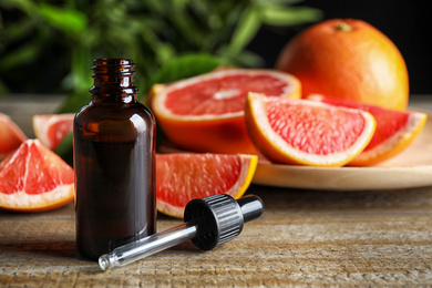 Photo of Citrus essential oil and grapefruits on wooden table. Space for text