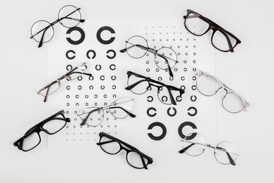 Photo of Vision test charts and glasses on white background, flat lay