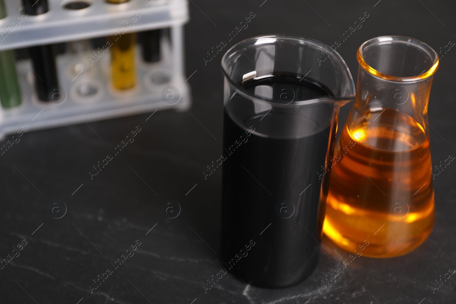 Photo of Beaker and flask with different types of oil on grey textured table, closeup. Space for text