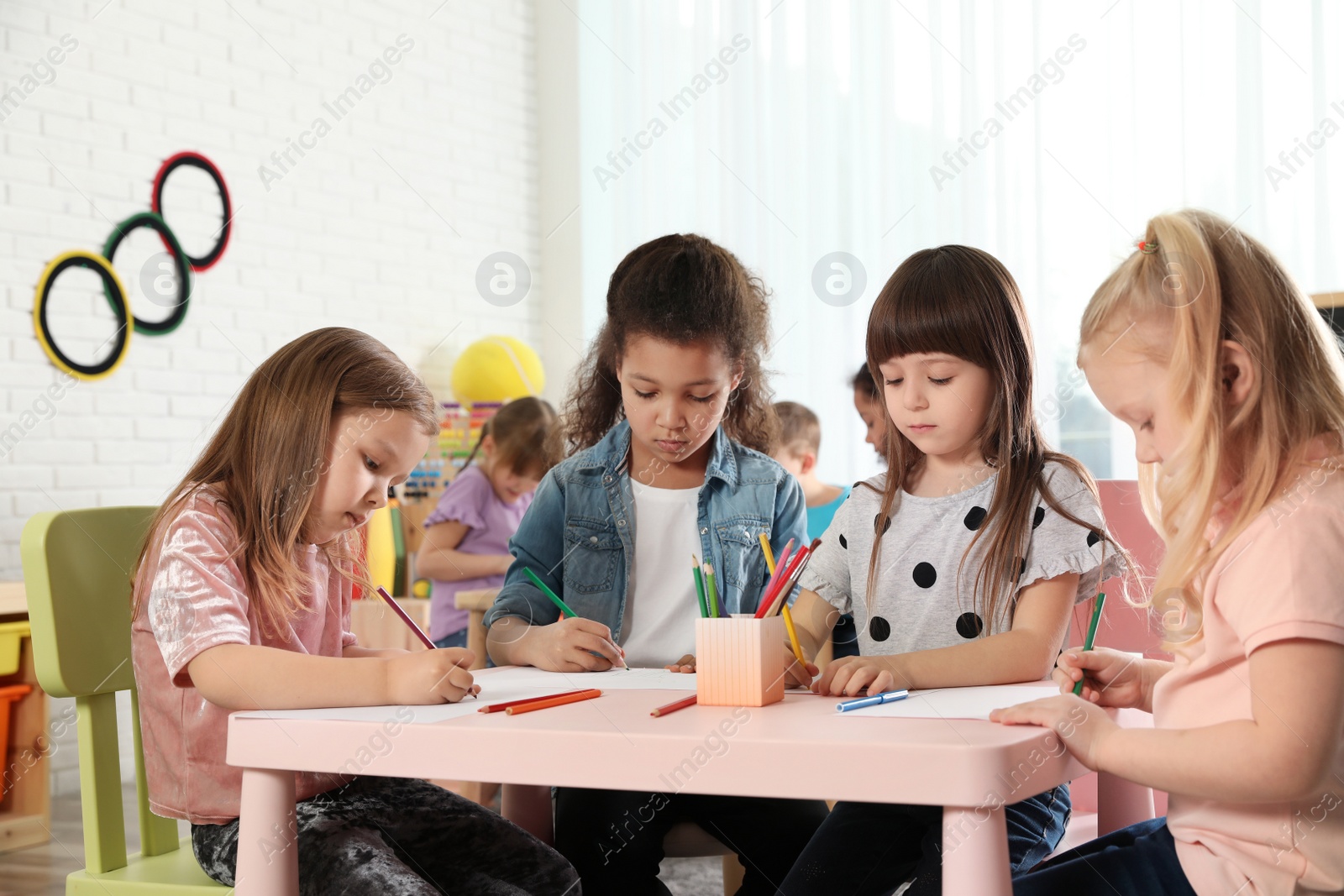 Photo of Adorable children drawing together at table indoors. Kindergarten playtime activities