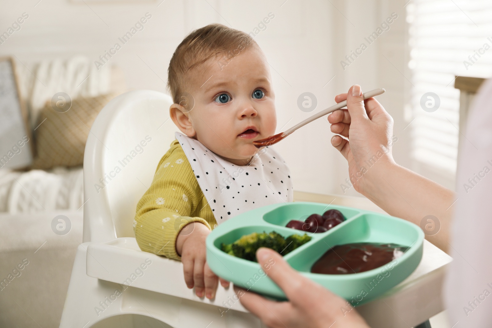 Photo of Mother feeding her little baby at home. Kid wearing bib