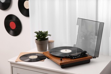 Stylish turntable on white chest of drawers and vinyl records indoors