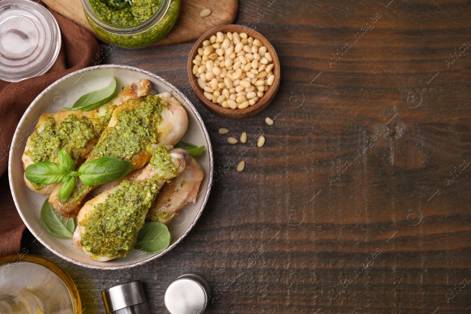 Photo of Delicious fried chicken drumsticks with pesto sauce and ingredients on wooden table, flat lay. Space for text