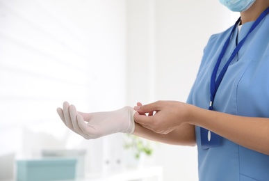 Photo of Doctor putting on medical gloves against blurred background, closeup
