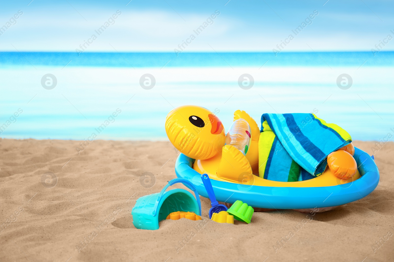 Photo of Set of plastic beach toys and inflatable duck with towel on sand near sea. Space for text