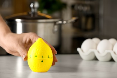 Photo of Woman winding up kitchen timer in shape of lemon at table indoors