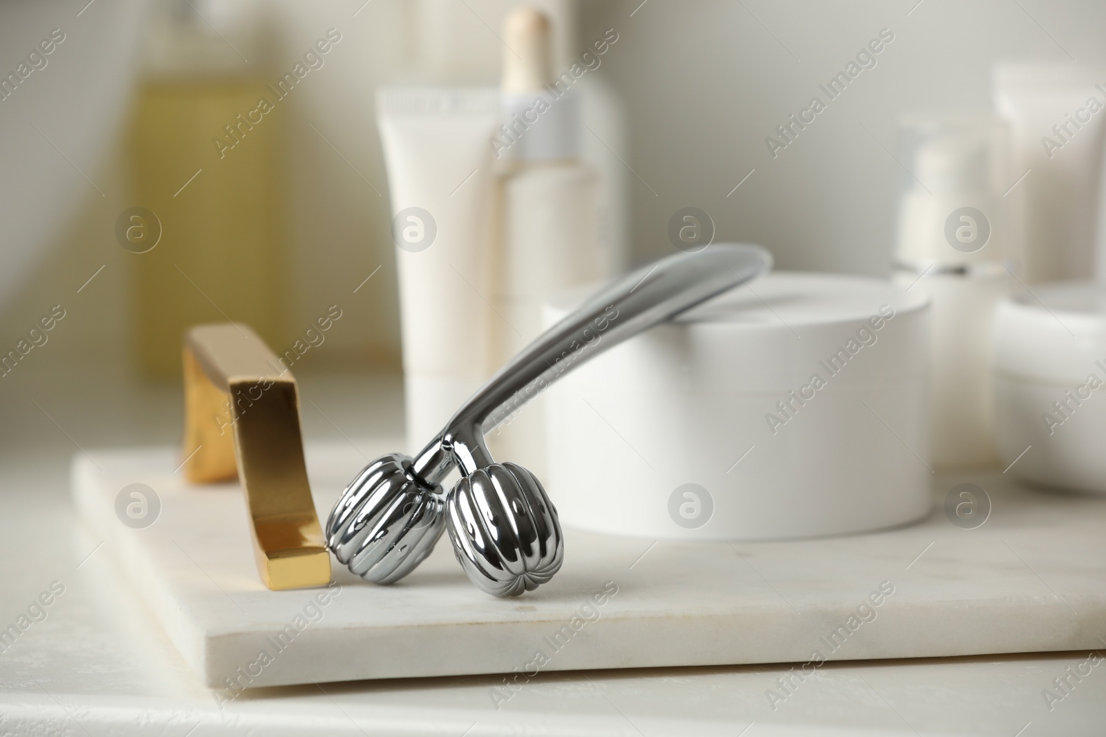 Photo of Tray with metal face roller and cosmetic products on counter in bathroom, closeup