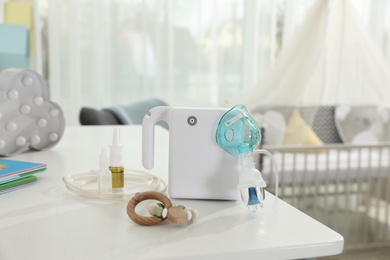 Photo of Modern nebulizer, medicines and wooden baby toy on white table in children's room. Equipment for inhalation