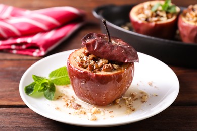 Tasty baked apple with nuts, honey and mint on wooden table, closeup