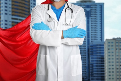 Image of Doctor dressed as superhero on city background, closeup. Medical workers fighting with dangerous diseases