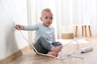 Photo of Little child playing with electrical socket and power strip plug at home. Dangerous situation