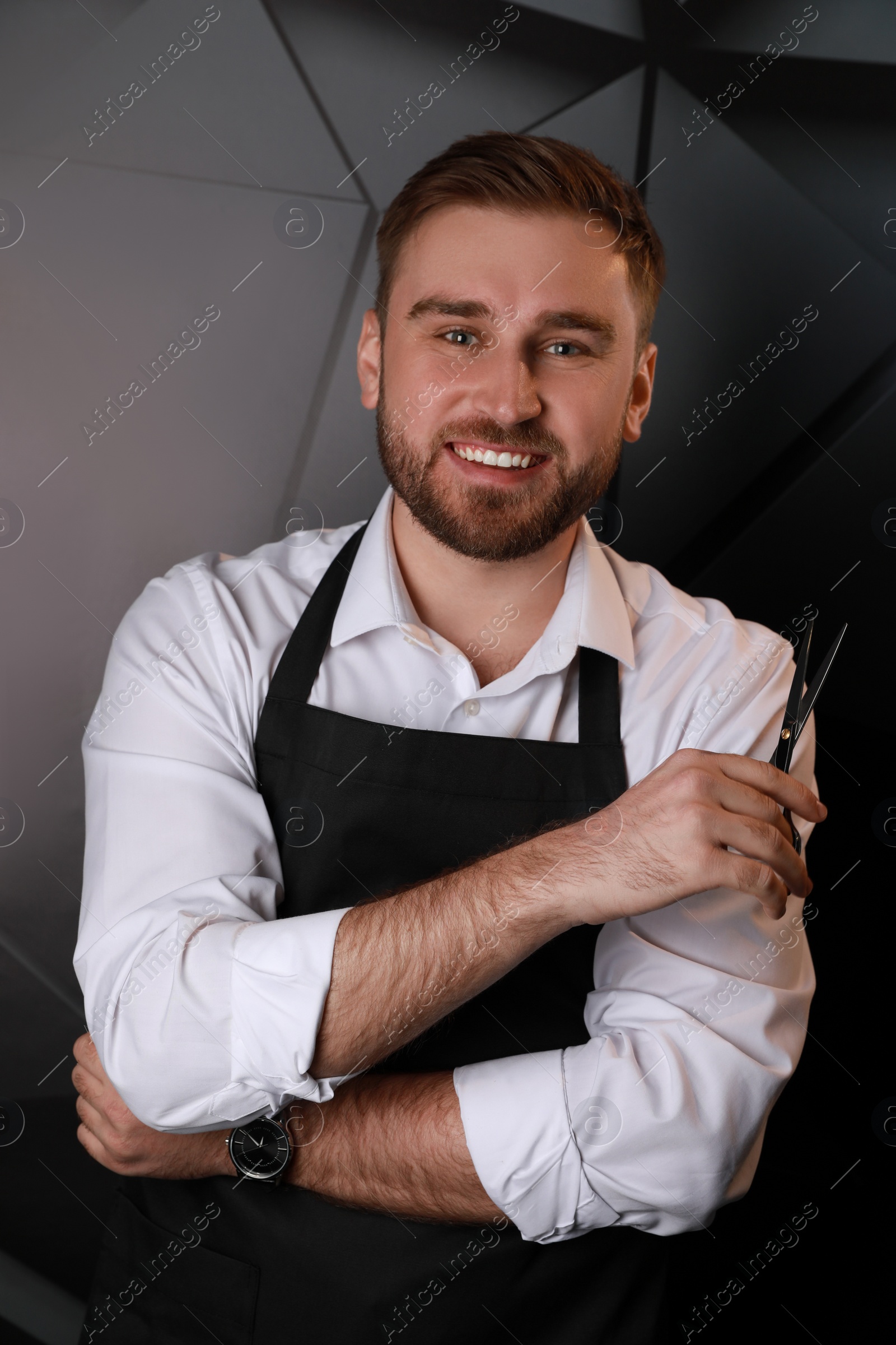 Photo of Happy hairdresser with professional scissors on dark background