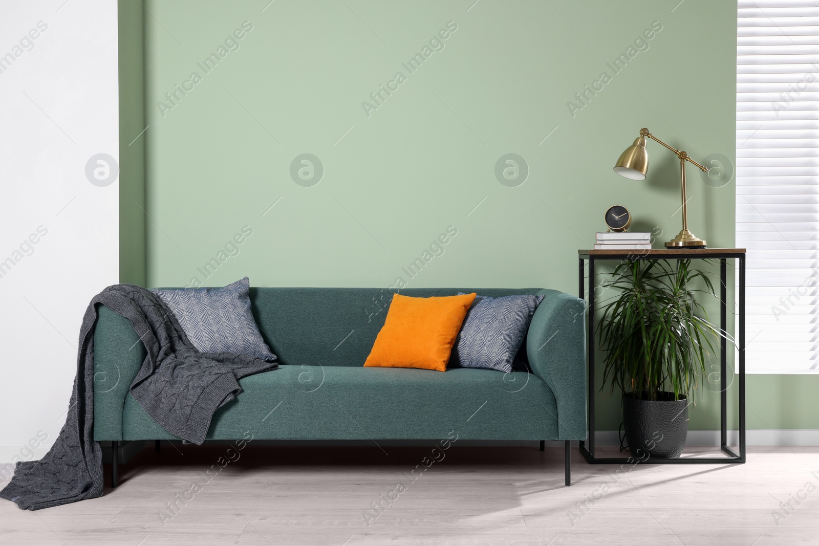 Photo of Stylish interior with comfortable sofa, blanket and cushions near console table