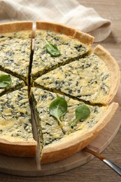 Cut delicious spinach pie with server on wooden table