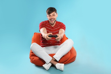 Emotional man playing video games with controller on color background