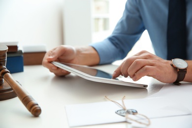 Photo of Notary working with tablet at table in office, closeup. Law and justice concept