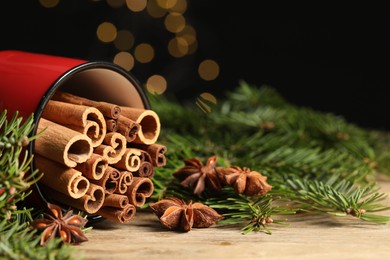 Many cinnamon sticks, anise stars and fir branches on wooden table, closeup. Space for text