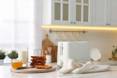 Photo of Breakfast served in kitchen. Toaster, crunchy bread, honey and milk on white marble table