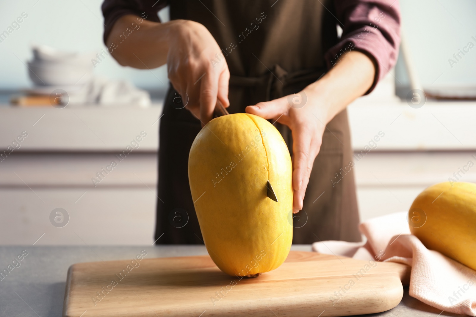 Photo of Woman cutting spaghetti squash on table in kitchen, closeup