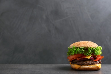 Photo of Tasty burger with bacon on table against grey background, space for text