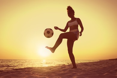 African American woman playing football on beach at sunset