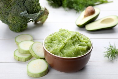 Photo of Bowl with tasty puree, zucchini, avocado and broccoli on white wooden table