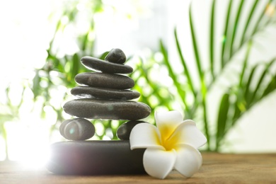 Table with stack of stones, flower and blurred green leaves on background, space for text. Zen concept