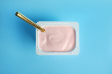 Photo of Tasty organic yogurt with spoon on light blue background, top view