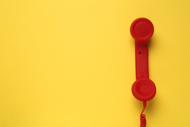Photo of Red corded telephone handset on yellow background, top view. Hotline concept