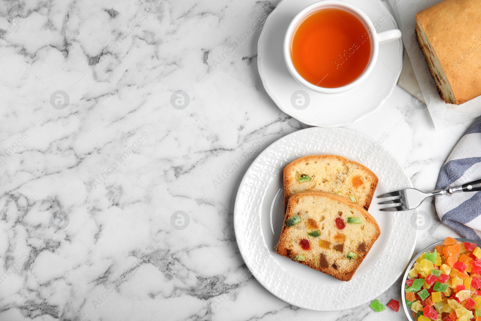 Photo of Delicious cake with candied fruits and tea on white marble table, flat lay. Space for text