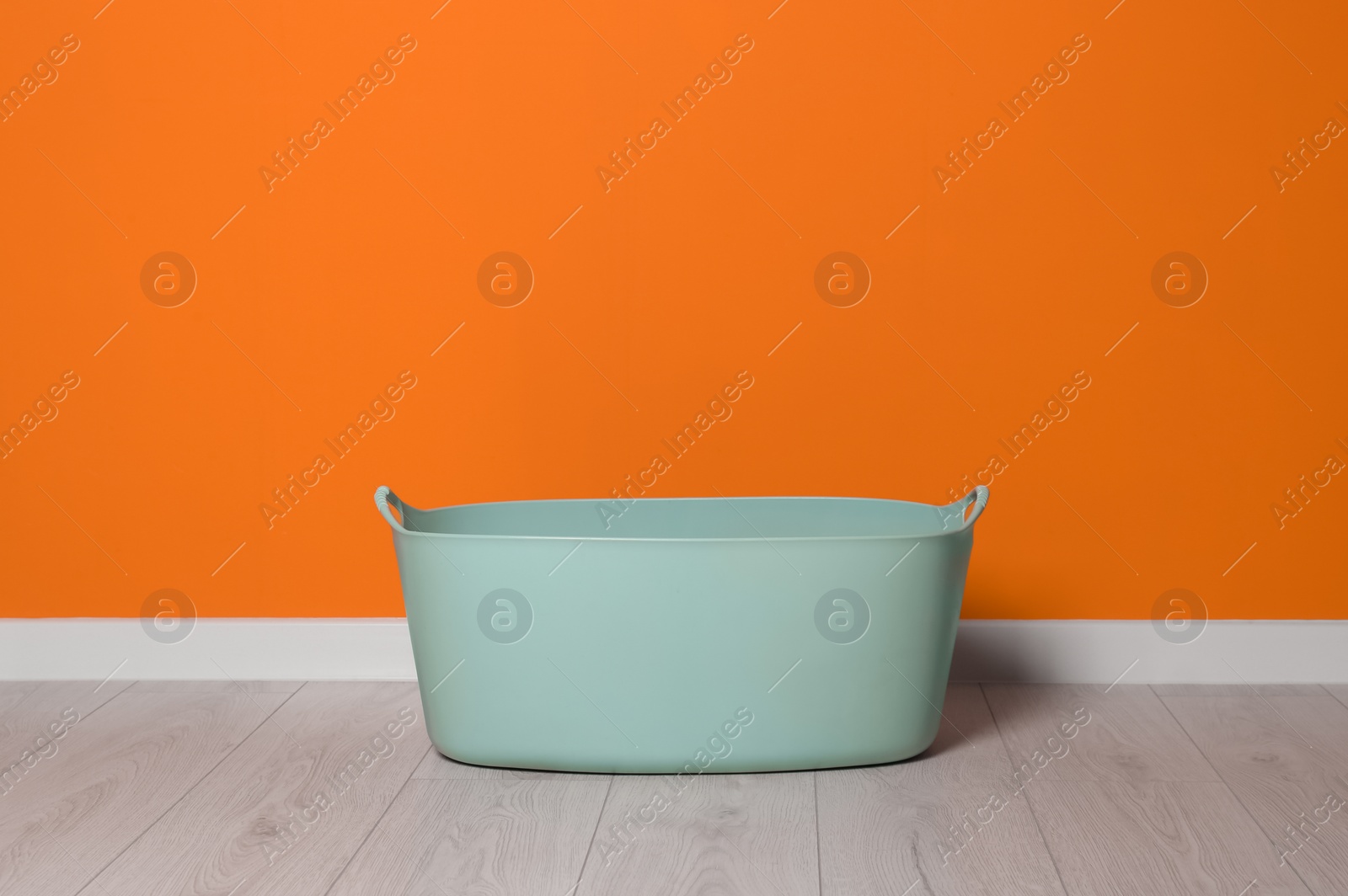 Photo of Laundry basket with handles near orange wall indoors, space for text