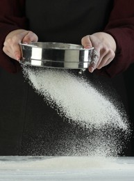 Woman sieving flour at table against black background, closeup