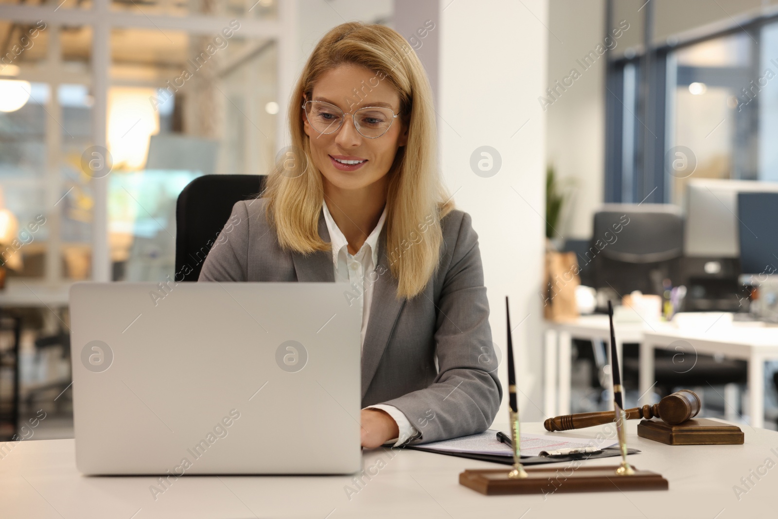 Photo of Smiling lawyer working with laptop at table in office