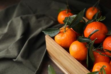 Photo of Wooden crate with fresh ripe tangerines and leaves on table, closeup. Space for text