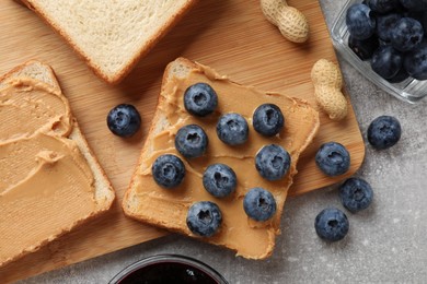 Photo of Tasty peanut butter sandwiches with fresh blueberries and peanuts on gray table, flat lay