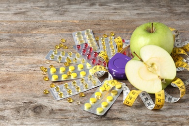 Weight loss pills with apples and measuring tape on wooden background