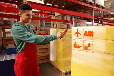 Image of Worker wrapping boxes with shipping icons in stretch film at warehouse