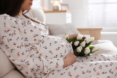 Photo of Young pregnant woman with flowers at home, closeup